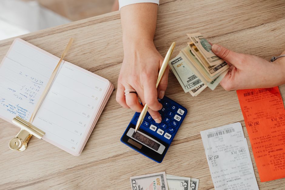 Hands managing finances with calculator, cash, and receipts on a wooden table. Ideal for budgeting concepts.